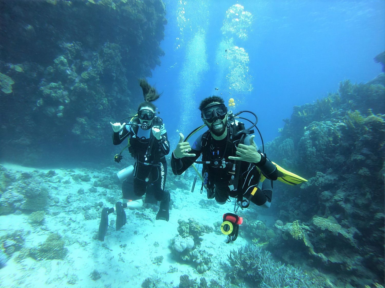 Two divers signalling OK beside the reef in sunlit water